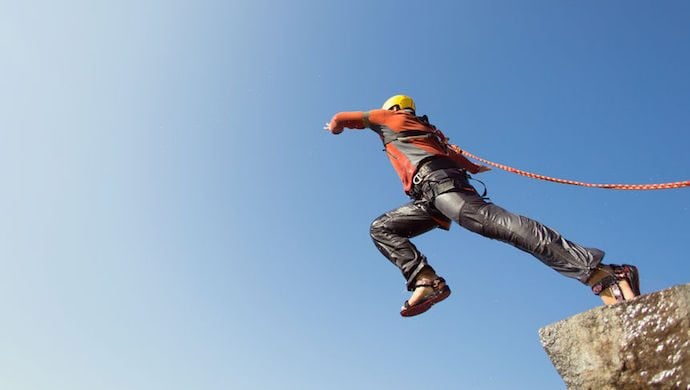 57918890 - man jumping off a cliff with a rope on a sunny day.