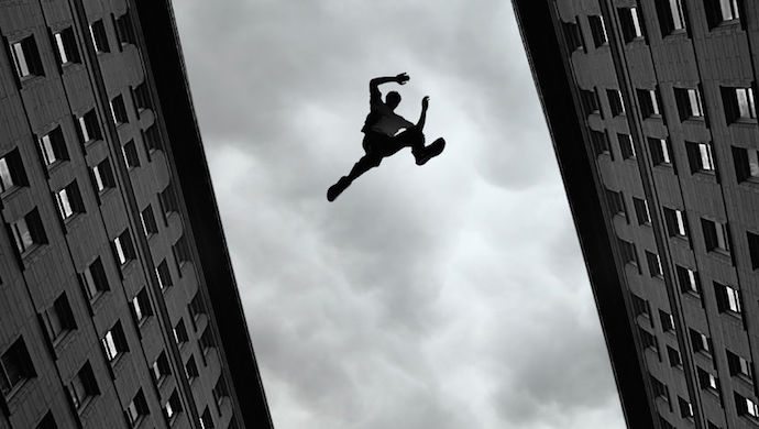 37963179 - man jumping over building roof against gray sky background