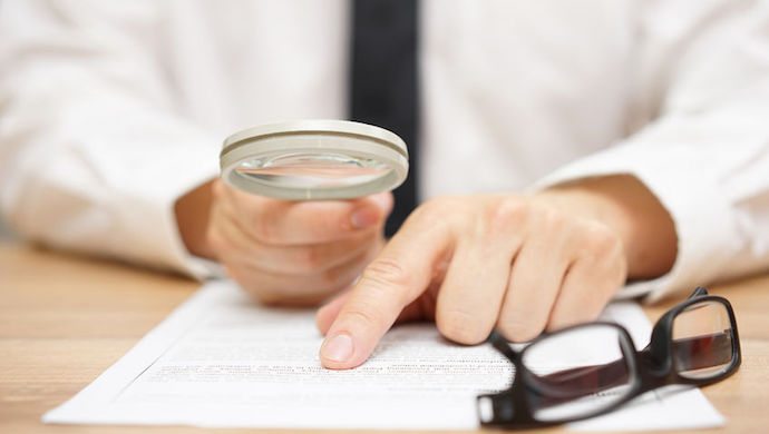 47708428 - focused businessman is reading through  magnifying glass document